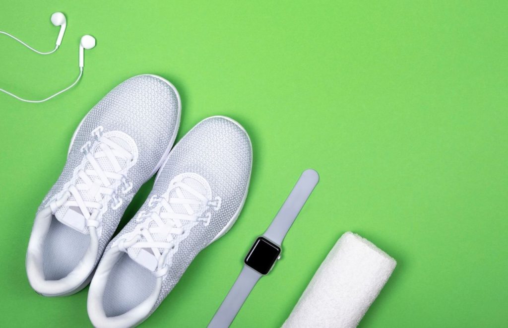 White sneakers with apple watch white towel and headphones on green background Canva