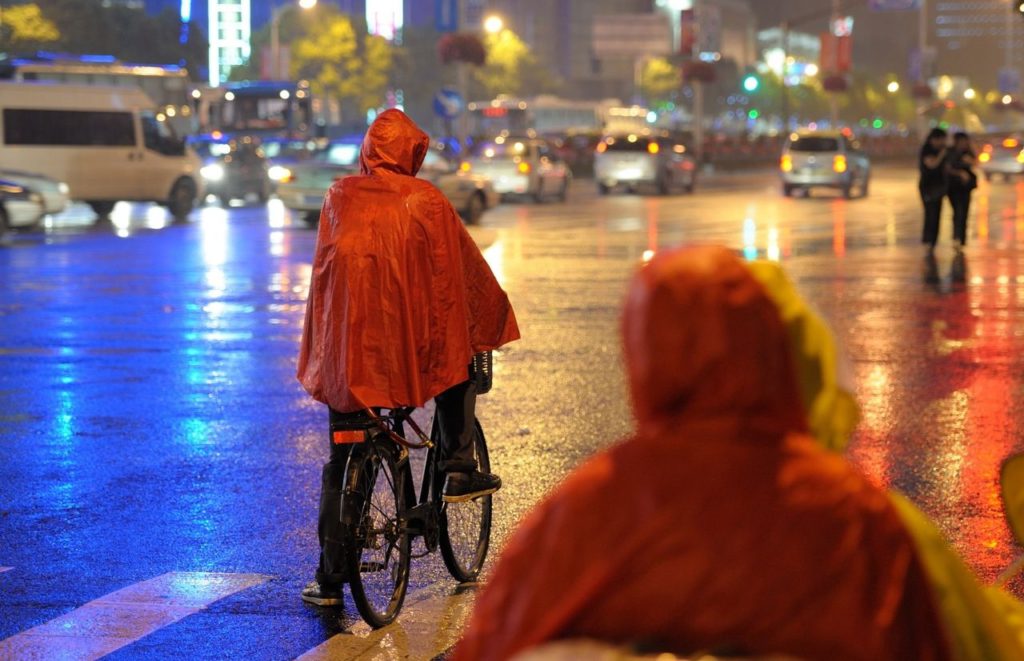 Person on bike in the city at night with Red Rain Poncho. Keep reading to get the best rain ponchos for travel to Florida.